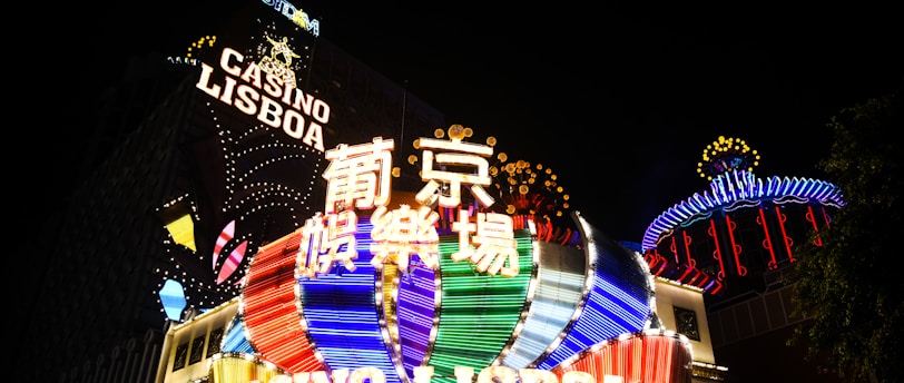 Bright neon signs in multiple colors illuminate the night, prominently displaying the name 'Casino Lisboa' alongside signage in Chinese characters. The lights form intricate patterns and vibrant displays, creating a lively and energetic atmosphere.